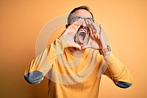 Middle age hoary man wearing casual sweater and glasses over isolated yellow background Shouting angry out loud with hands over