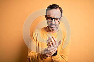 Middle age hoary man wearing casual sweater and glasses over isolated yellow background Suffering pain on hands and fingers,