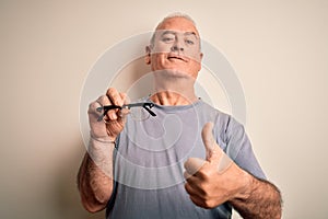 Middle age hoary optical man holding vision glasses over isolated white background happy with big smile doing ok sign, thumb up