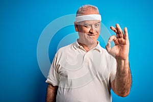 Middle age hoary sportsman doing sport wearing sportswear over isolated blue background smiling positive doing ok sign with hand