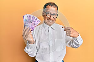 Middle age indian man holding 100 philippine peso banknotes smiling happy pointing with hand and finger