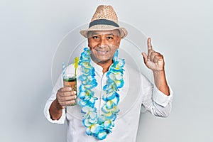 Middle age latin man wearing summer style drinking mojito glass surprised with an idea or question pointing finger with happy