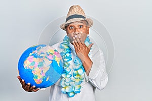 Middle age latin man wearing summer style holding world ball covering mouth with hand, shocked and afraid for mistake