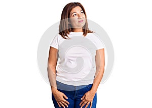 Middle age latin woman wearing casual white tshirt smiling looking to the side and staring away thinking