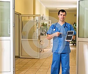 Middle age male doctor in blue scrubs holding and pointing to tablet with NHS text photo