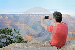 Middle age male tourist making mobile photo of the famous Grand Canyon from Mather Point. Handsome man traveling and admiring