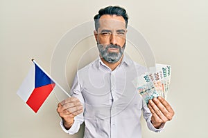 Middle age man with beard and grey hair holding czech republic flag and koruna banknotes depressed and worry for distress, crying