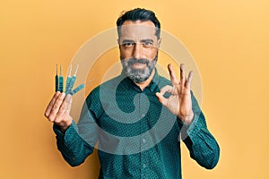 Middle age man with beard and grey hair holding picklock to unlock security door doing ok sign with fingers, smiling friendly
