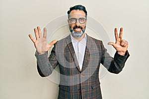 Middle age man with beard and grey hair wearing business jacket and glasses showing and pointing up with fingers number eight