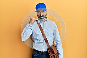 Middle age man with beard and grey hair wearing delivery courier cap smiling doing phone gesture with hand and fingers like