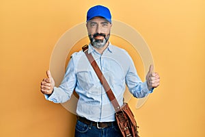 Middle age man with beard and grey hair wearing delivery courier cap success sign doing positive gesture with hand, thumbs up