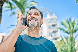 Middle age man with beard smiling happy outdoors speaking on the phone