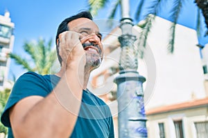 Middle age man with beard smiling happy outdoors speaking on the phone