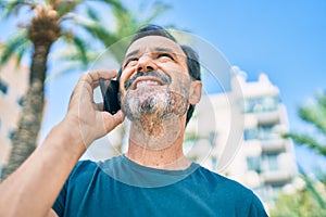 Middle age man with beard smiling happy outdoors speaking on the phone