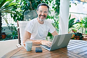 Middle age man with beard smiling happy at the terrace working from home using laptop