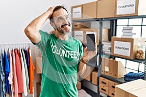 Middle age man with beard wearing volunteer t shirt holding smartphone smiling confident touching hair with hand up gesture,