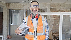 Middle age man builder smiling confident holding hardhat at construction site