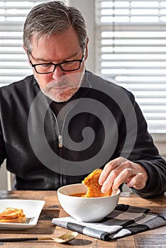 Middle age man dipping a grilled cheese sandwich in a bowl of soup