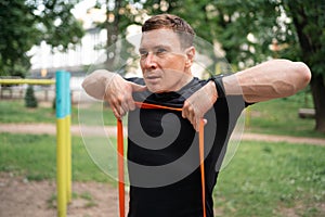 Middle age man doing strength exercises with resistance bands outdoors in park