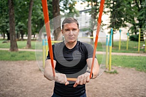 Middle age man doing strength exercises with resistance bands outdoors in park