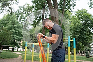 Middle age man doing strength exercises with resistance bands outdoors in park