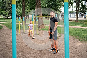 Middle age man doing strength exercises with resistance bands outdoors in park with child girl daughter