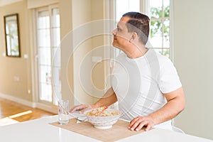 Middle age man eating rice at home looking to side, relax profile pose with natural face with confident smile