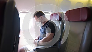Middle age man in face mask traveling by an airplane. Passenger fastens the seat belt in aircraft during flight. Safety