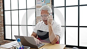 Middle age man with grey hair business worker talking on the phone using laptop at office