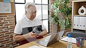 Middle age man with grey hair business worker using laptop putting headphones on at office