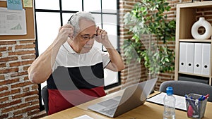 Middle age man with grey hair business worker using laptop putting headphones on at office