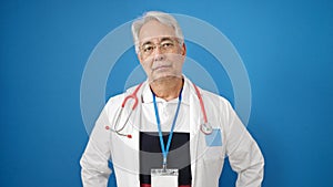 Middle age man with grey hair doctor standing with serious expression over isolated blue background