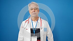 Middle age man with grey hair doctor standing with serious expression over isolated blue background