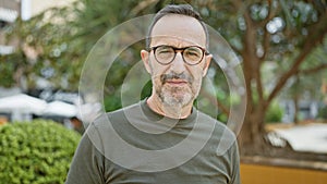 Middle age man with grey hair, a serious expression whilst standing in a city park, revealing the nature of a thinking, outdoors