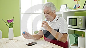 Middle age man with grey hair sitting on the table drinking water at dinning room