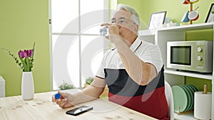 Middle age man with grey hair sitting on the table drinking water at dinning room