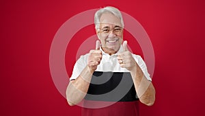 Middle age man with grey hair smiling with thumbs up over isolated red background