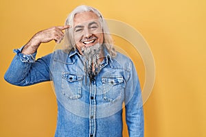 Middle age man with grey hair standing over yellow background smiling pointing to head with one finger, great idea or thought,