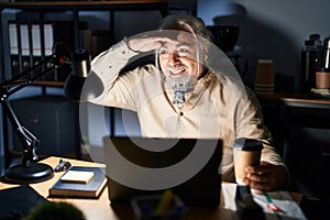 Middle age man with grey hair working at the office at night very happy and smiling looking far away with hand over head