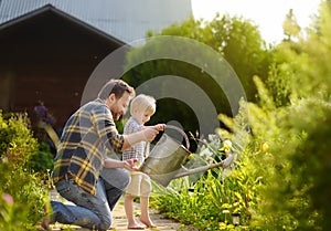 Middle age man and his little son watering flowers in the garden at summer sunny day