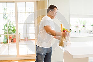 Middle age man holding grocieries bag full of vegetables at home