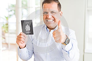 Middle age man holding holding Canadian passport happy with big smile doing ok sign, thumb up with fingers, excellent sign