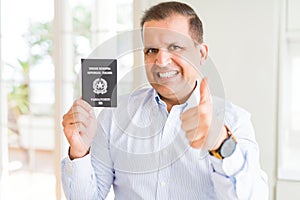 Middle age man holding holding passport of Italy happy with big smile doing ok sign, thumb up with fingers, excellent sign