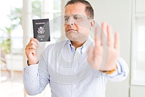 Middle age man holding holding passport of United States with open hand doing stop sign with serious and confident expression,