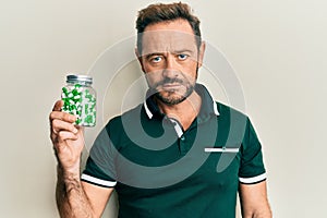 Middle age man holding pills thinking attitude and sober expression looking self confident