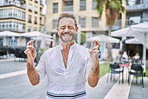 Middle age man outdoor at the city gesturing finger crossed smiling with hope and eyes closed