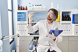 Middle age man scientist looking test tube holding clipboard at laboratory