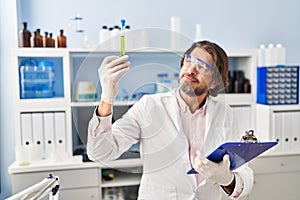 Middle age man scientist looking test tube holding clipboard at laboratory
