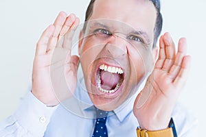 Middle age man shouting crazy with hands over mouth over white wall background