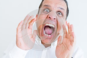 Middle age man shouting crazy with hands over mouth over white wall background